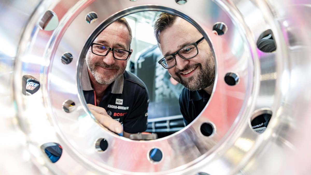 Two men are looking through a wheel rim that has been polished to a high shine.